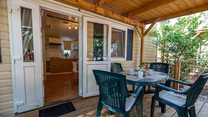 Un área de comedor al aire libre techada con mesa y sillas, una terraza de madera y vistas a la cocina contigua.