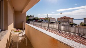 Un balcon avec une table et des chaises, donnant sur un parking et un plan d’eau.