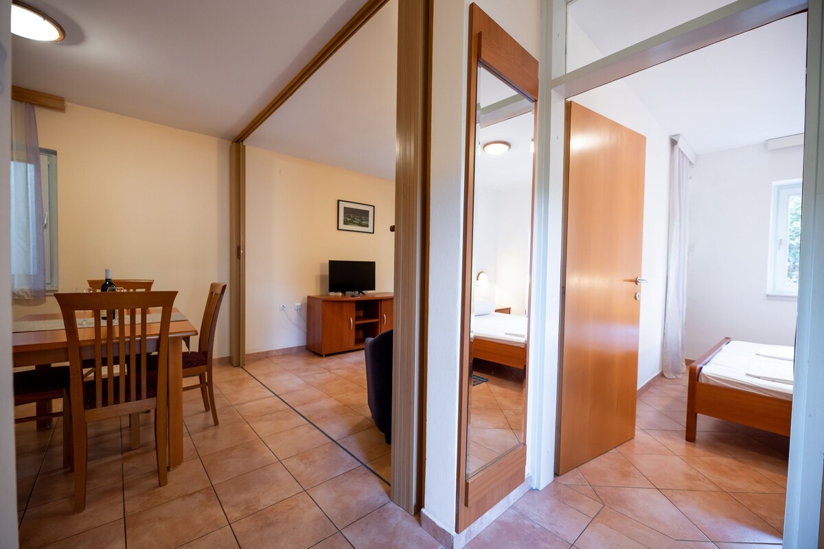 A room with a bed, a desk, and a chair. There is a television on a wooden cabinet.