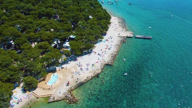 Ett flygbildsbild av ett kustområde med en strand, klart turkosfärgat vatten och båtar.