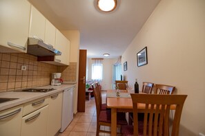 A compact kitchen with a stove, sink, and cabinets, leading to a dining area with wooden chairs and a table.
