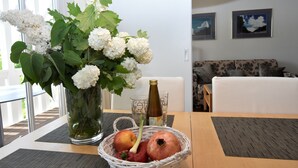 Een eettafel met een vaas witte bloemen, een mand vol fruit en een fles wijn.