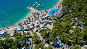 Luftaufnahme eines Küstenresorts mit Schwimmbad, Strand und einem Stellplatz für Wohnmobile.