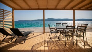 Eine Holzterrasse mit Tisch und Stühlen mit Blick auf Strand und Meer.