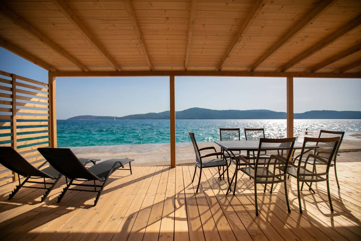 Een houten terras met tafel en stoelen, met uitzicht op een strand en zee.