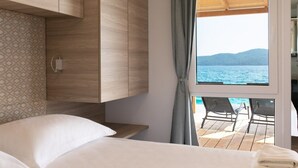 Ein Schlafzimmer mit einem Bett, einem Holzschrank, einem Fenster mit Meerblick und einem Balkon mit Stühlen.