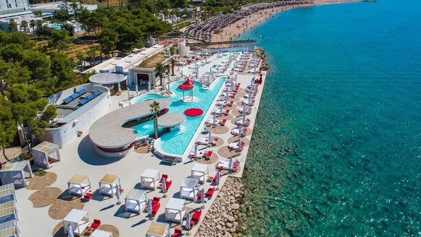 Ein Resort mit großem Schwimmbecken, Liegestühlen und einem Strand.