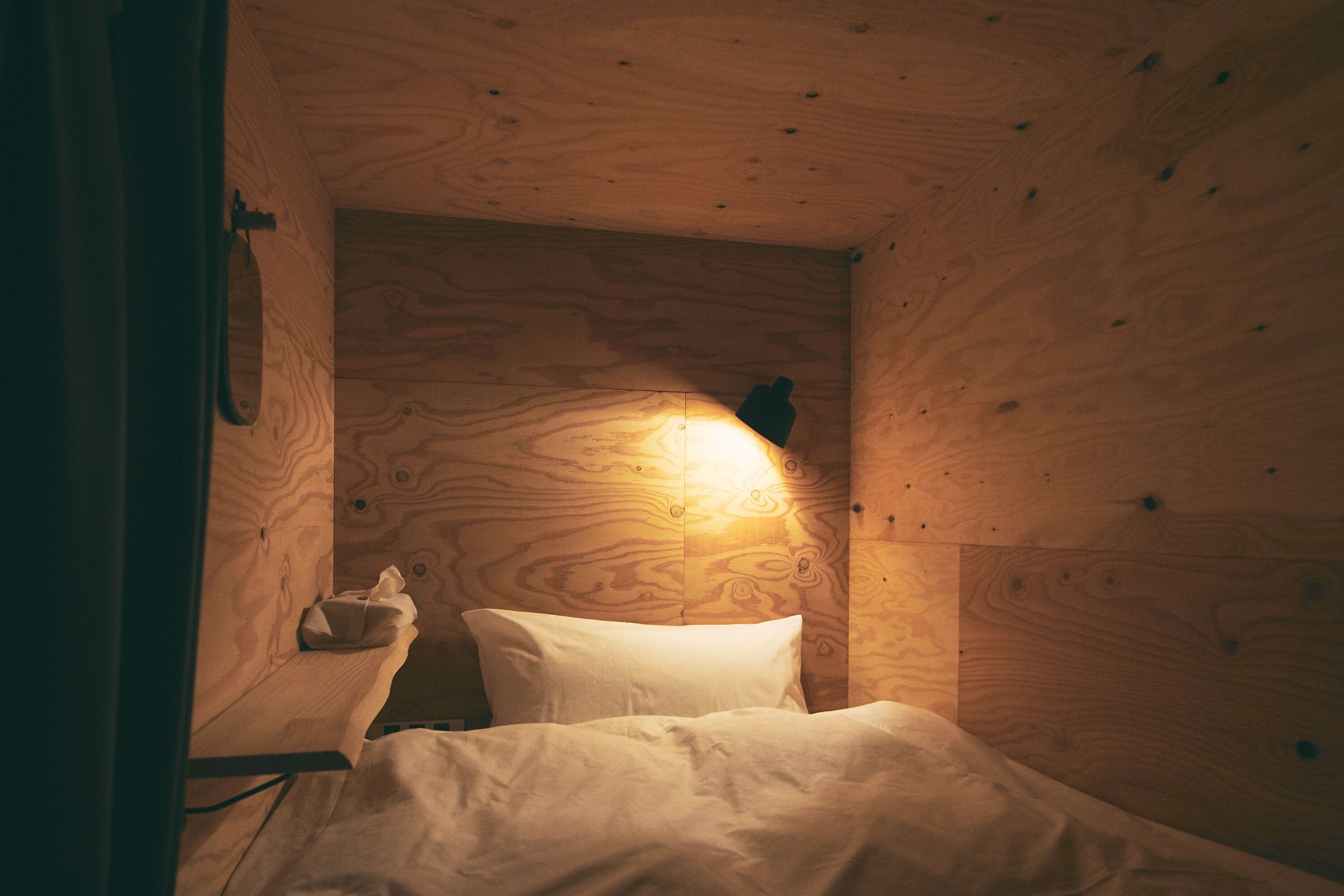 A wooden cabin room with a bed, a nightstand, and a wall-mounted lamp.