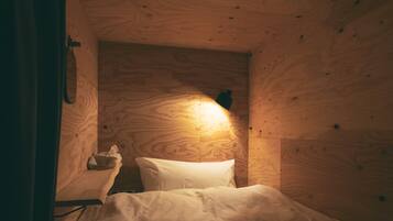 A wooden cabin room with a bed, a nightstand, and a wall-mounted lamp.