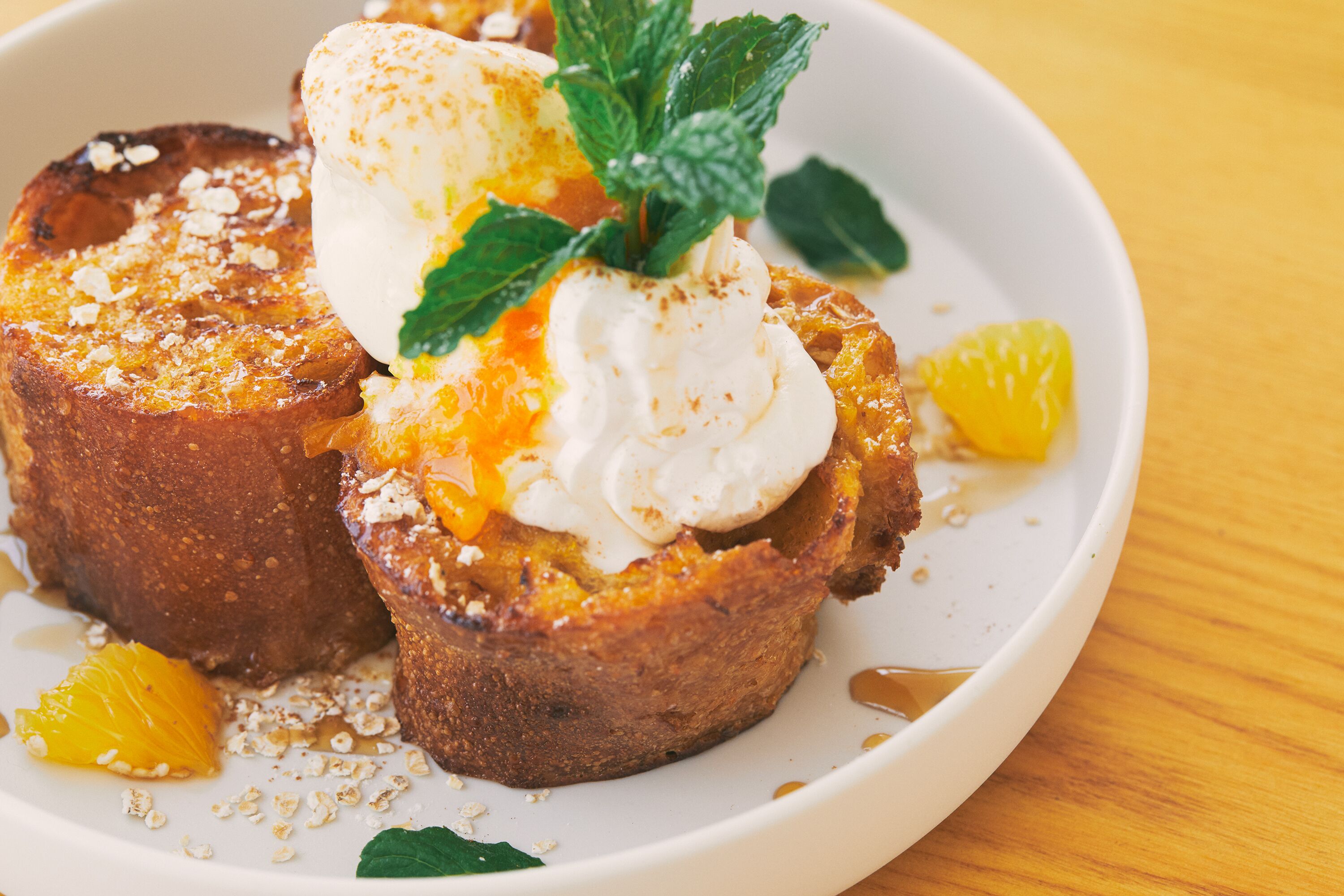 Une assiette de pain perdu, garnie d’un œuf poché, de tranches d’orange et d’une feuille de menthe.