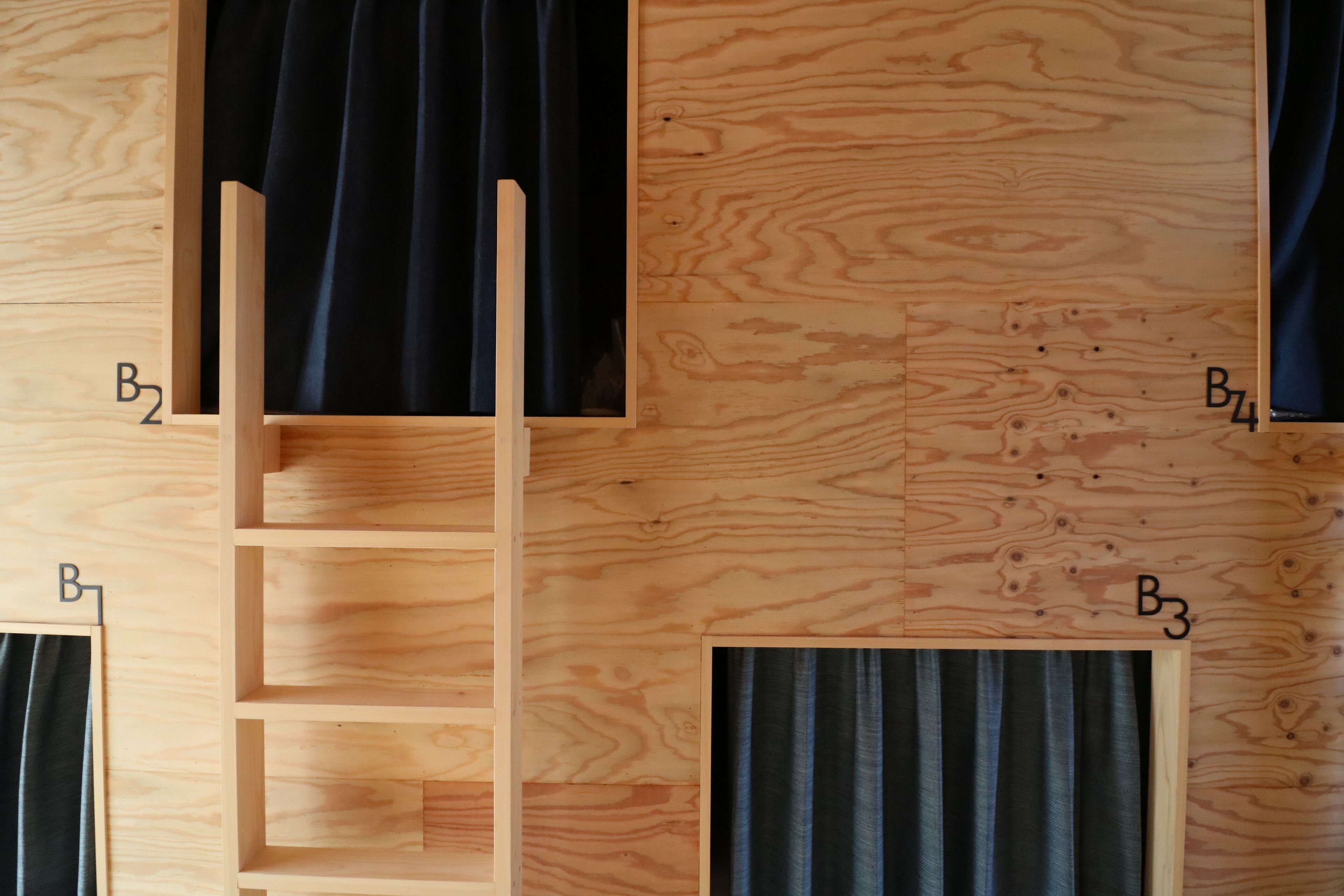 Een houten kamer met een ingebouwde ladder en twee ramen voorzien van gordijnen.