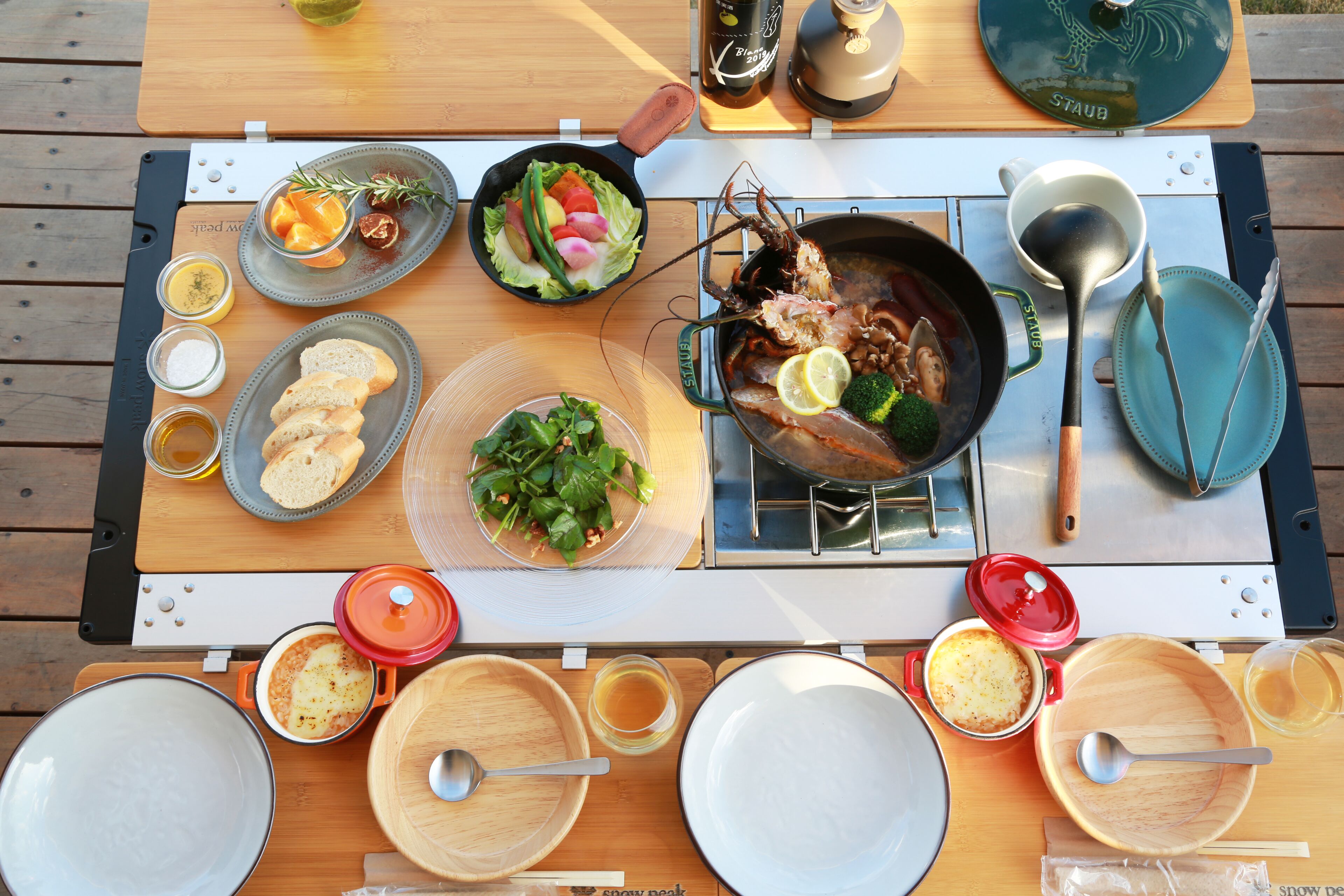 A wooden table set with various dishes, including a pan of seafood, salads, and bread.