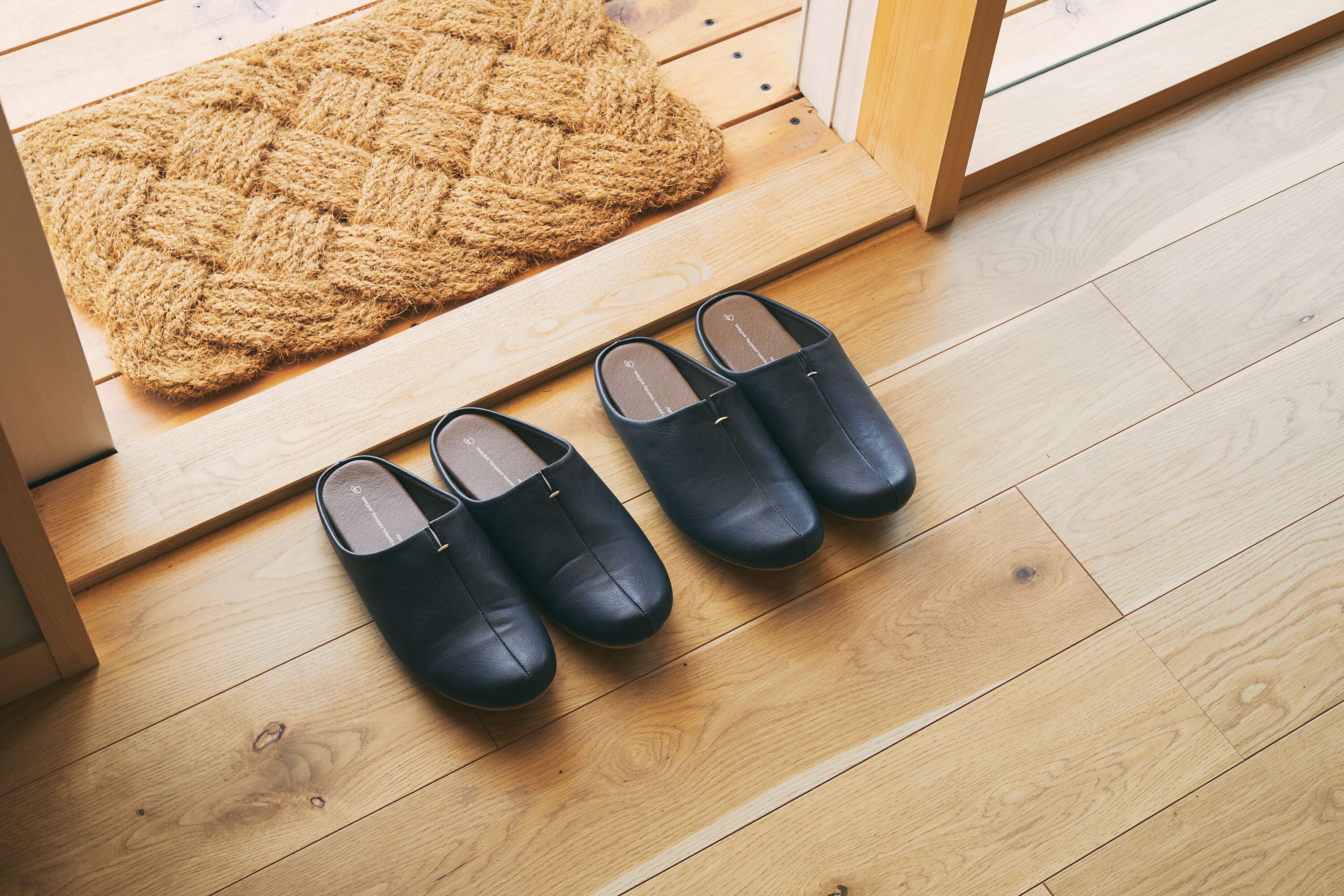 A wooden floor with a doormat and a pair of black shoes.