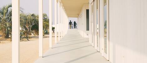 A long, covered corridor with white walls and doors, leading to a building.