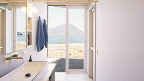 Un baño con lavamanos, espejo y barra para toallas. Tiene vista a una playa y una montaña al fondo.