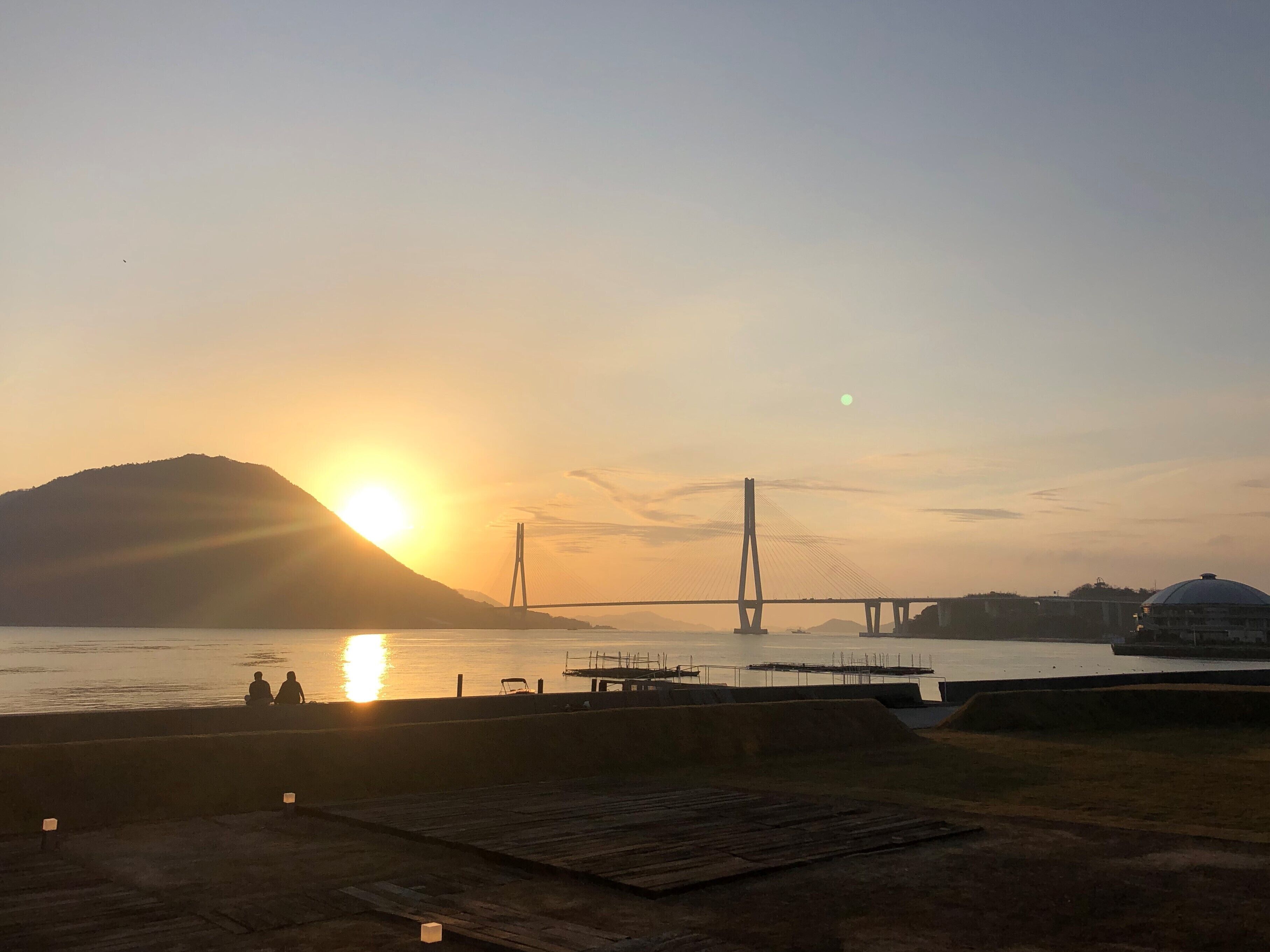 A sunset view with a bridge and a hill in the background.