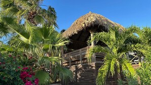 A wooden structure with a thatched roof, surrounded by palm trees and pink flowers. - Villa in Jan Thiel With Private Pool (Jan Thiel)