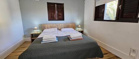 Una camera da letto con un letto, pavimento in legno, una finestra con persiane e un condizionatore d'aria.