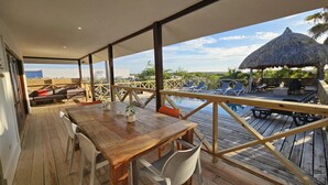 An outdoor deck with a wooden table and chairs, a pool, and lounge chairs under a thatched umbrella. - Villa in Jan Thiel With Private Pool (Jan Thiel)