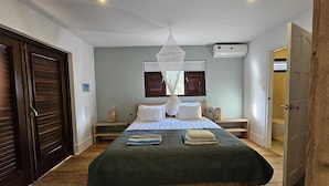 A bedroom with a large bed, wooden flooring, a ceiling fan, an air conditioning unit, and a door to the right. - Villa in Jan Thiel With Private Pool (Jan Thiel)