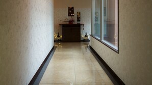 A hallway with patterned walls, a tiled floor, a ceiling with a geometric design, and a large window on the right. - Hotel Bintang Pari Resort - Adults Only (Kobe)