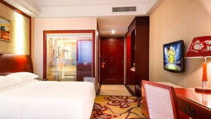 Habitación de hotel con cama, escritorio, televisor y puerta que da a un baño.
