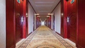 Un largo y estrecho pasillo con puertas rojas a ambos lados, alfombra estampada e iluminación empotrada en el techo.
