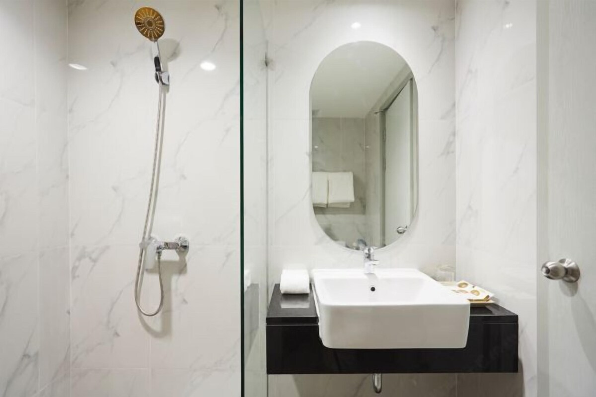 A modern bathroom with a marble wall, a white sink, a handheld showerhead, and a large mirror.