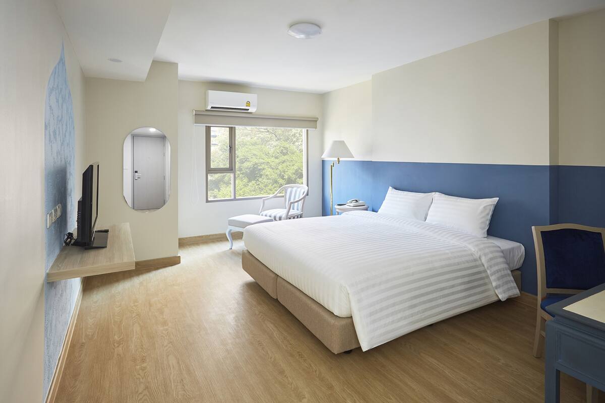 Habitació d'hotel amb un llit gran, escriptori, cadira, televisió i finestra que mostra vistes als arbres.