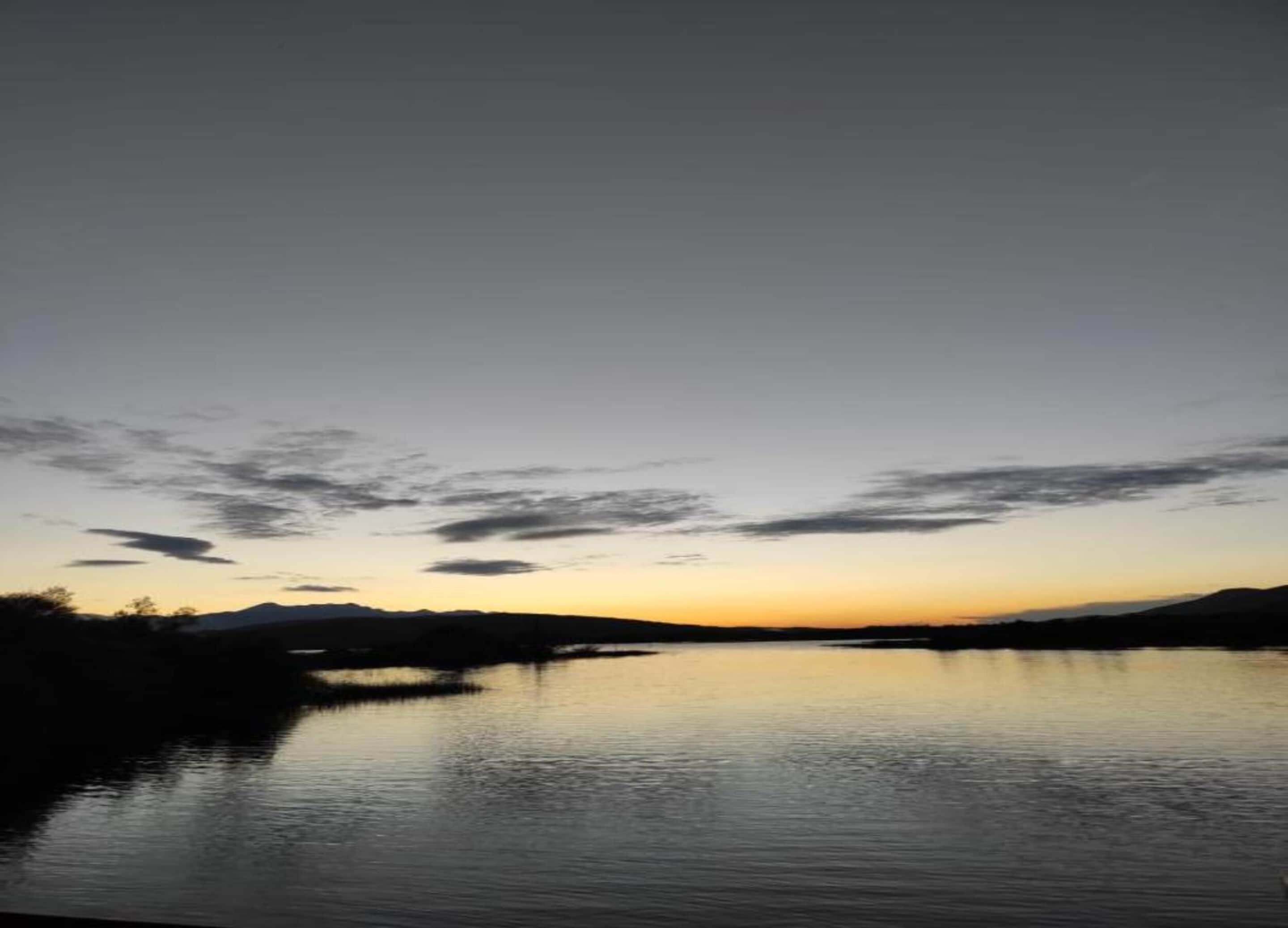 Un lac paisible au coucher du soleil, avec un ciel dégagé et des montagnes lointaines.