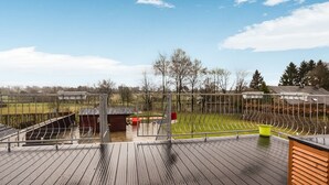 En træterrasse med et metalhegn, et lille skur og en græsplæne i baggrunden.