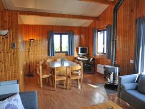 Ein Holzblockhaus-Interieur mit Esstisch, Stühlen, einer Couch, einem Fernseher und einem Kamin.