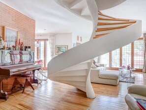 Un escalier en colimaçon dans un salon moderne, avec un piano, un canapé et de grandes fenêtres.
