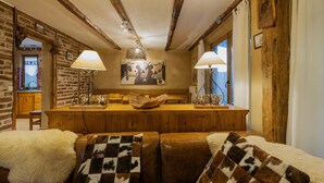 Un interior rústico con vigas de madera a la vista, una barra de madera y una zona de estar acogedora con un plaid de piel y cojines estampados.