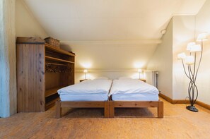 A wooden bed in a room with a sloped ceiling, a wooden wardrobe, and a floor lamp. - Chalet Retreat With Sauna (Waimes)