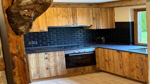 Una cocina con armarios de madera, salpicadero de baldosas negras y ventana con vistas al verdor.
