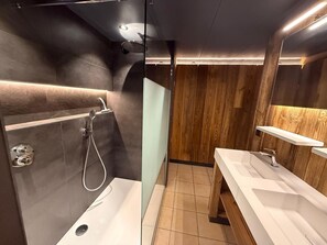 A modern bathroom with a glass-enclosed shower, a wooden wall panel, and a white vanity with a mirror. - Chalet Retreat With Sauna (Waimes)