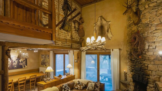 Un interior rústico con chimenea de piedra, muebles de madera y una pared de piedra decorada con cuernos de ciervo.