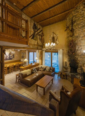 Un interior rústico con chimenea de piedra, muebles de madera y una pared de piedra decorada con cuernos de ciervo.
