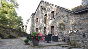 A stone building with a gravel courtyard, outdoor seating, and potted plants. - Renovated Mill in Bastogne Near Waterfall (Bastogne)