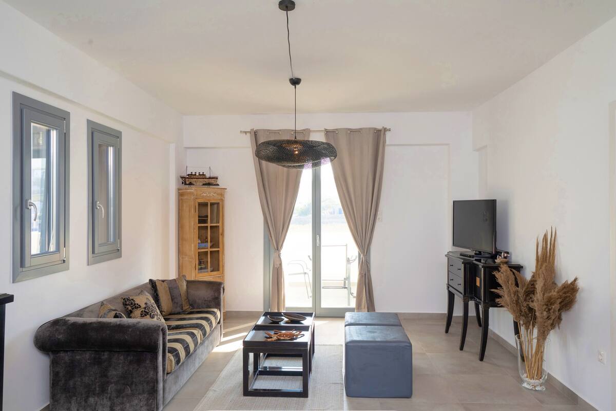 A living room with a sofa, a coffee table, a TV stand, and a large window with curtains.