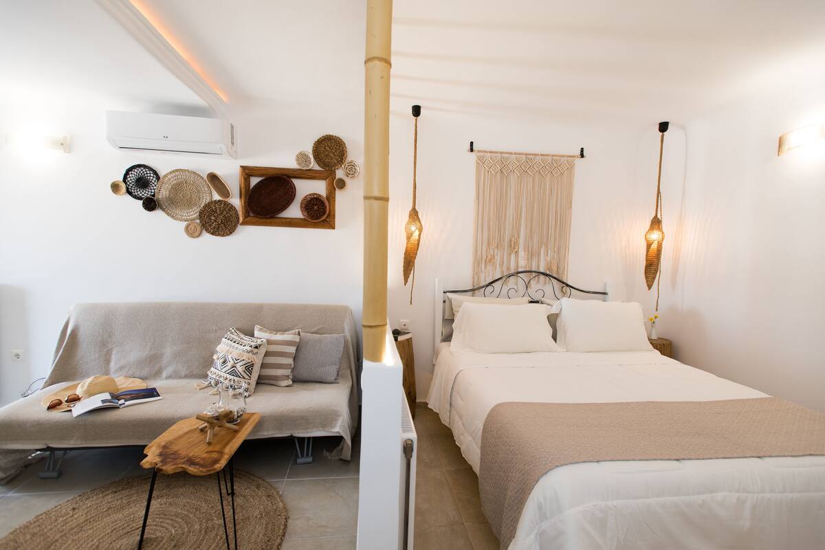 A hotel room with a sofa, a bed, a bedside table, and a wall-mounted air conditioner.