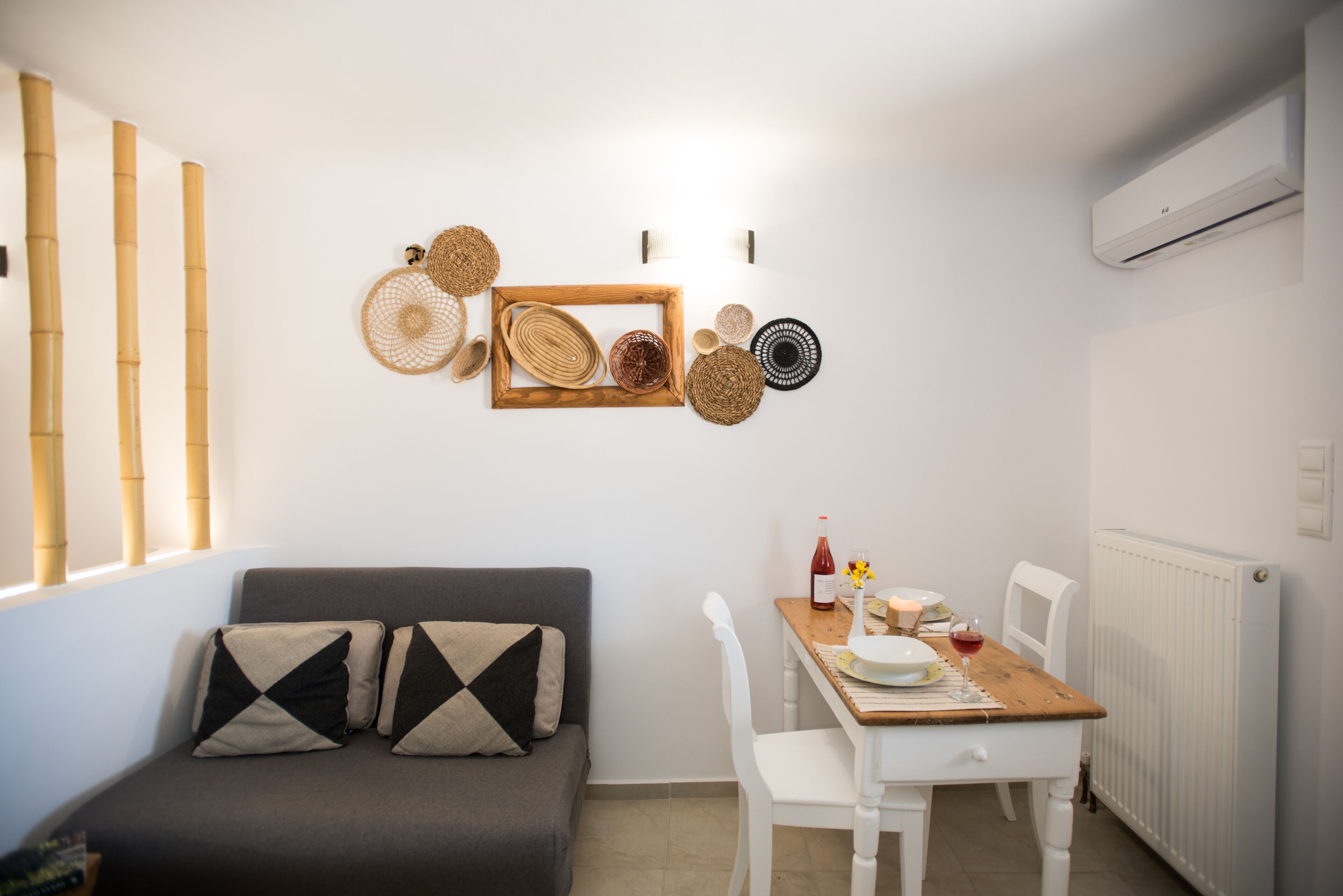 A small, well-lit room with a sofa, a dining table, and a wall decorated with woven baskets.
