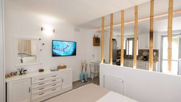 A modern bedroom with a large bed, a TV, a dresser, and a view into the kitchen.