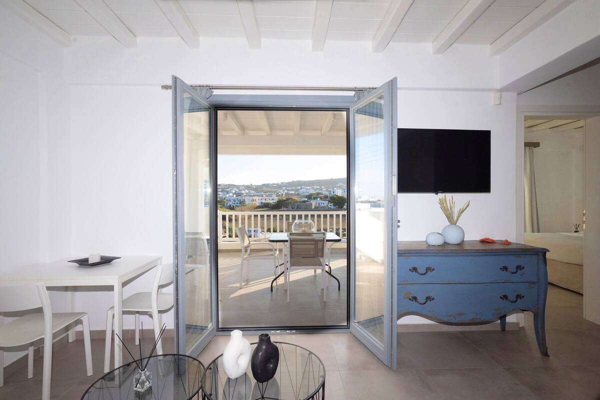 A modern room with a balcony, a dining area, and a TV mounted on the wall.