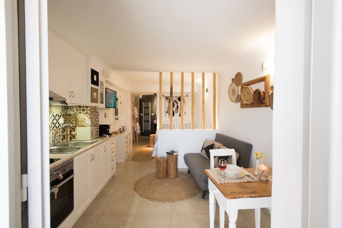 A compact kitchen with white cabinets, a stove, and a sink. There is a dining area with a table, chairs, and a small rug.