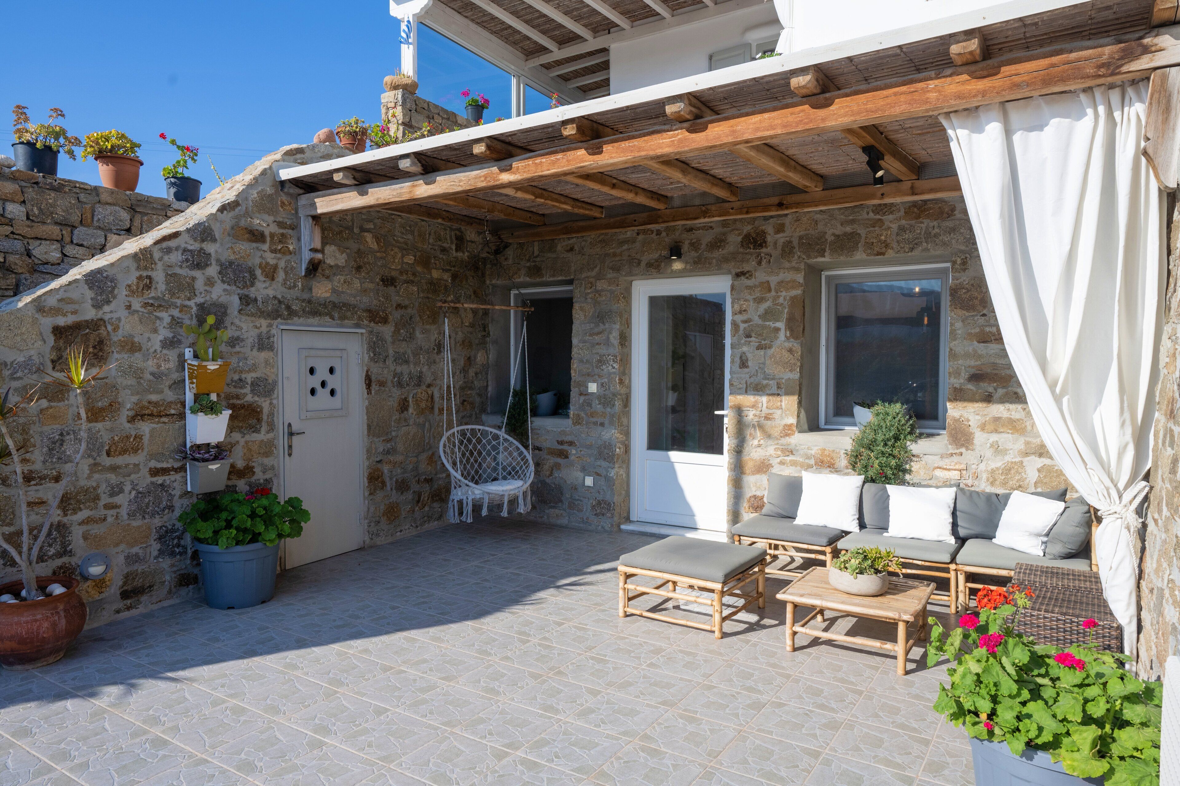 Un bâtiment en pierre doté d’un patio aménagé avec des meubles d’extérieur, un fauteuil suspendu et des plantes en pot.