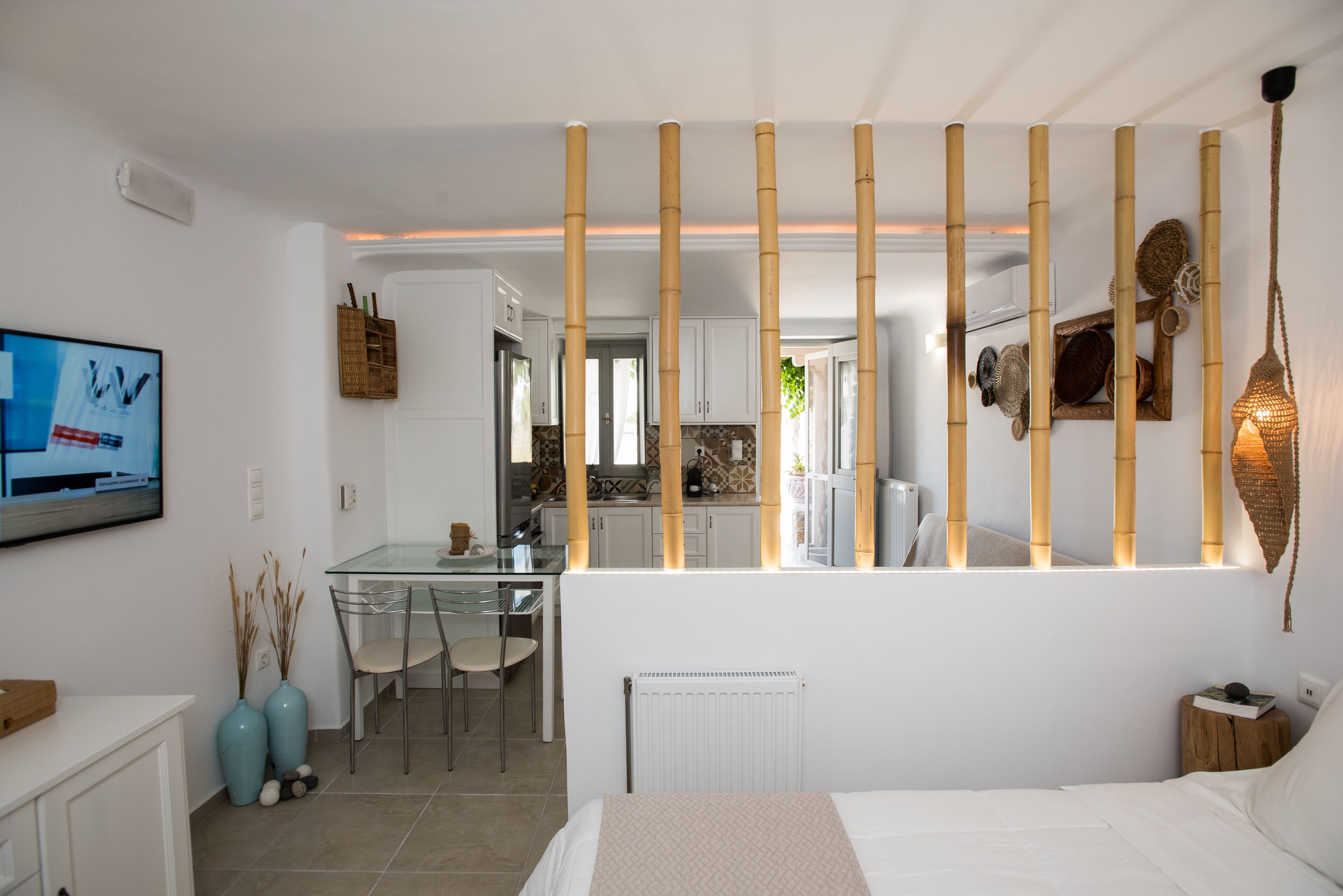 A modern bedroom with a bed, a desk, and a chair. There is a kitchen area visible through a glass partition.