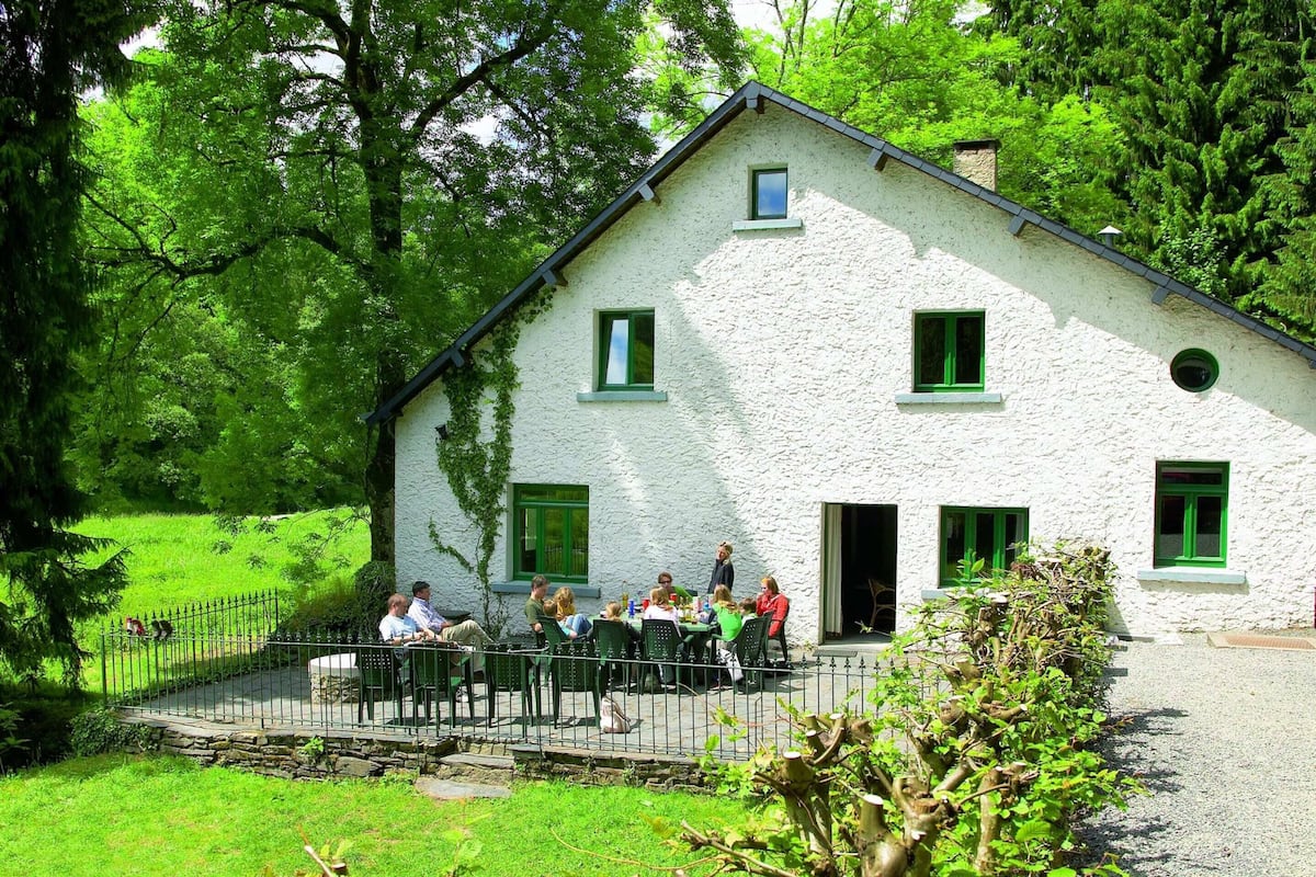 Un bâtiment blanc avec des volets verts, un porche en pierre et un chemin de gravier menant à l’entrée.
