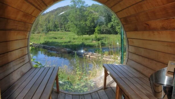 Een ronde kamer van hout met uitzicht op een rivier en bos.